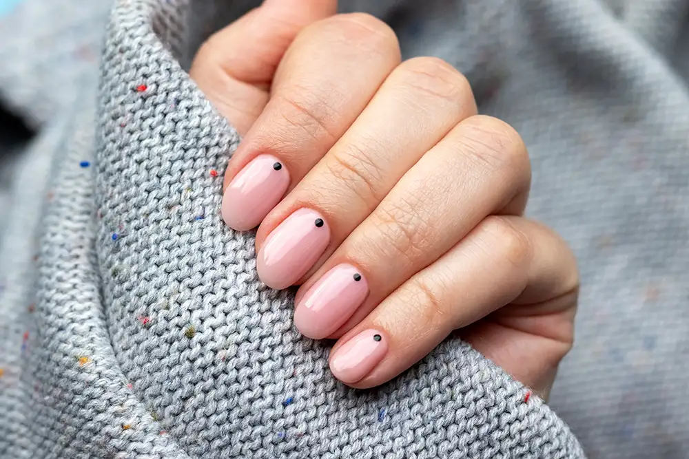 Weibliche Hand in einem grauen Strickpullover mit trendiger, schöner Maniküre – rosa Nude-Nägel mit kleinen schwarzen Punkten.